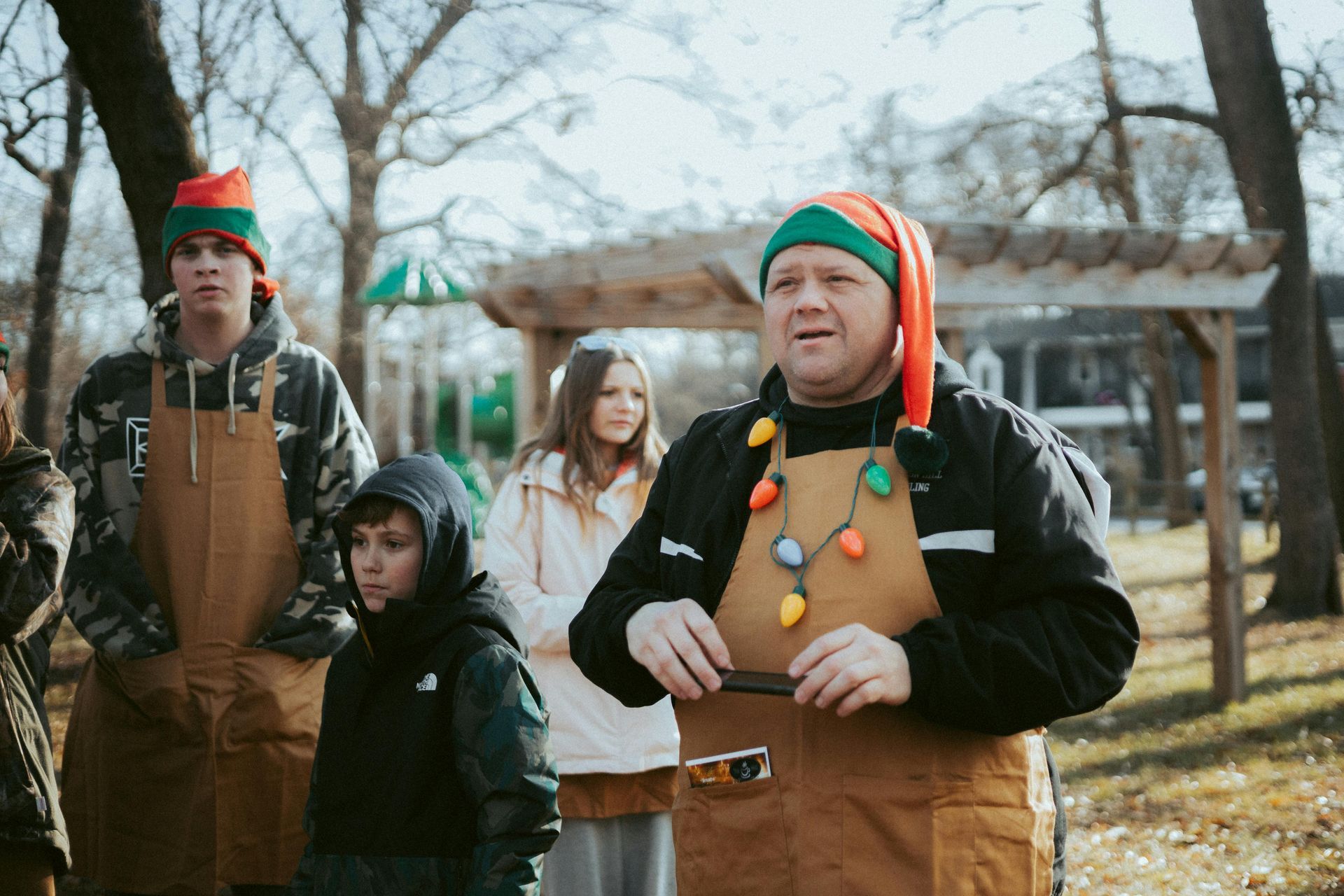 A group of people wearing elf hats and aprons, standing outside near a playground.