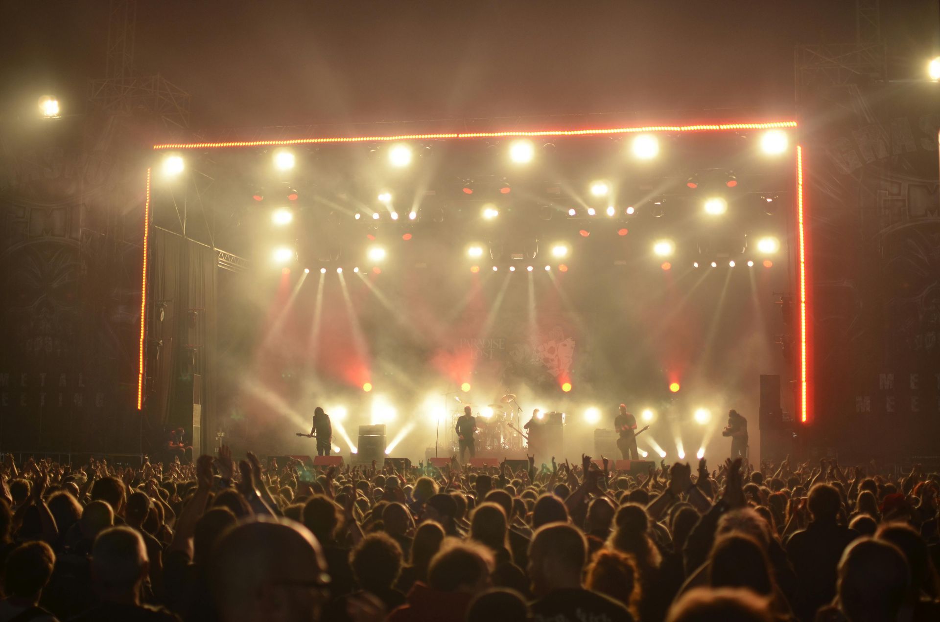 Concert crowd facing a brightly lit stage with red framing and haze