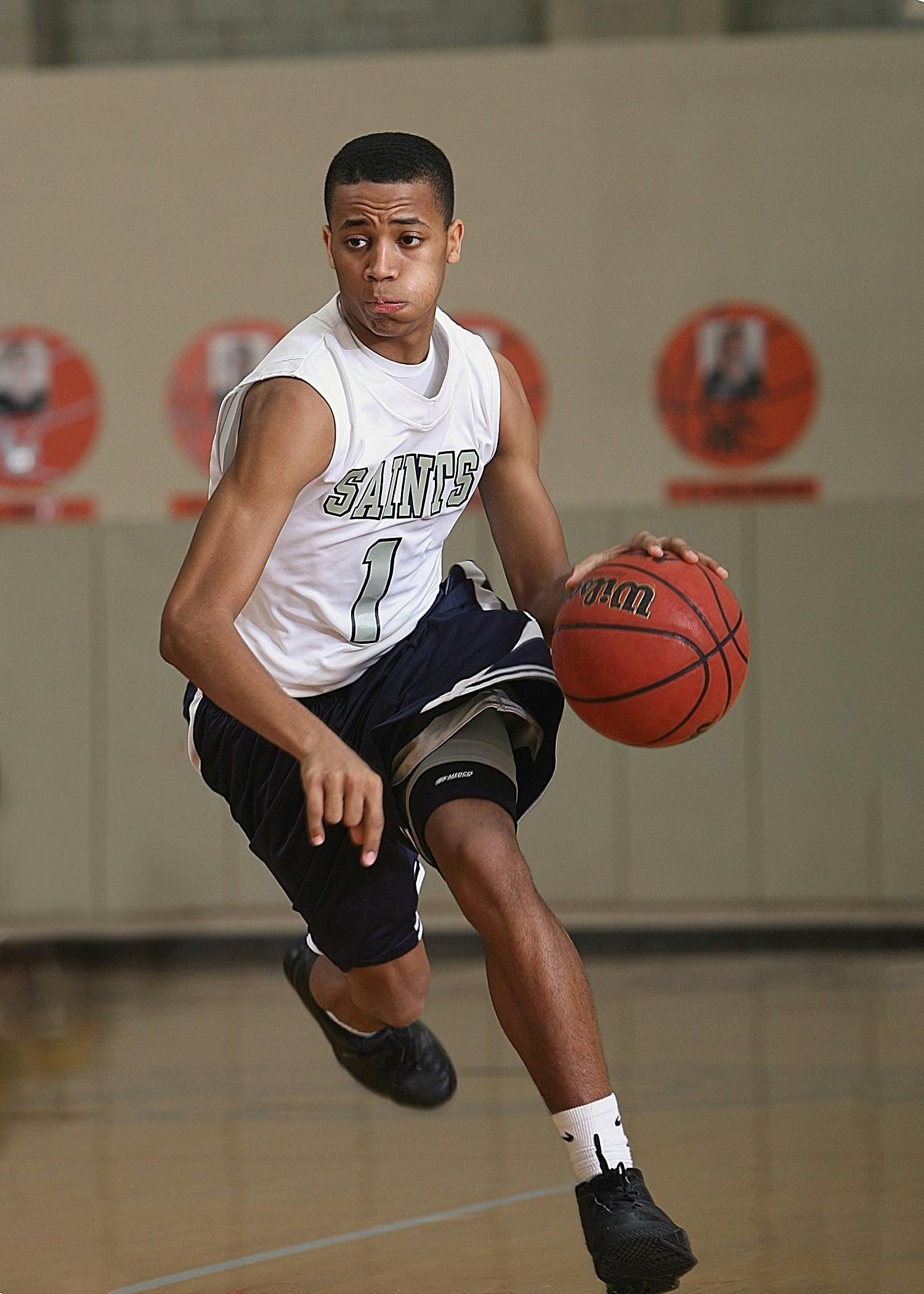 Basketball player dribbling a ball, wearing white jersey, navy shorts, and knee brace.