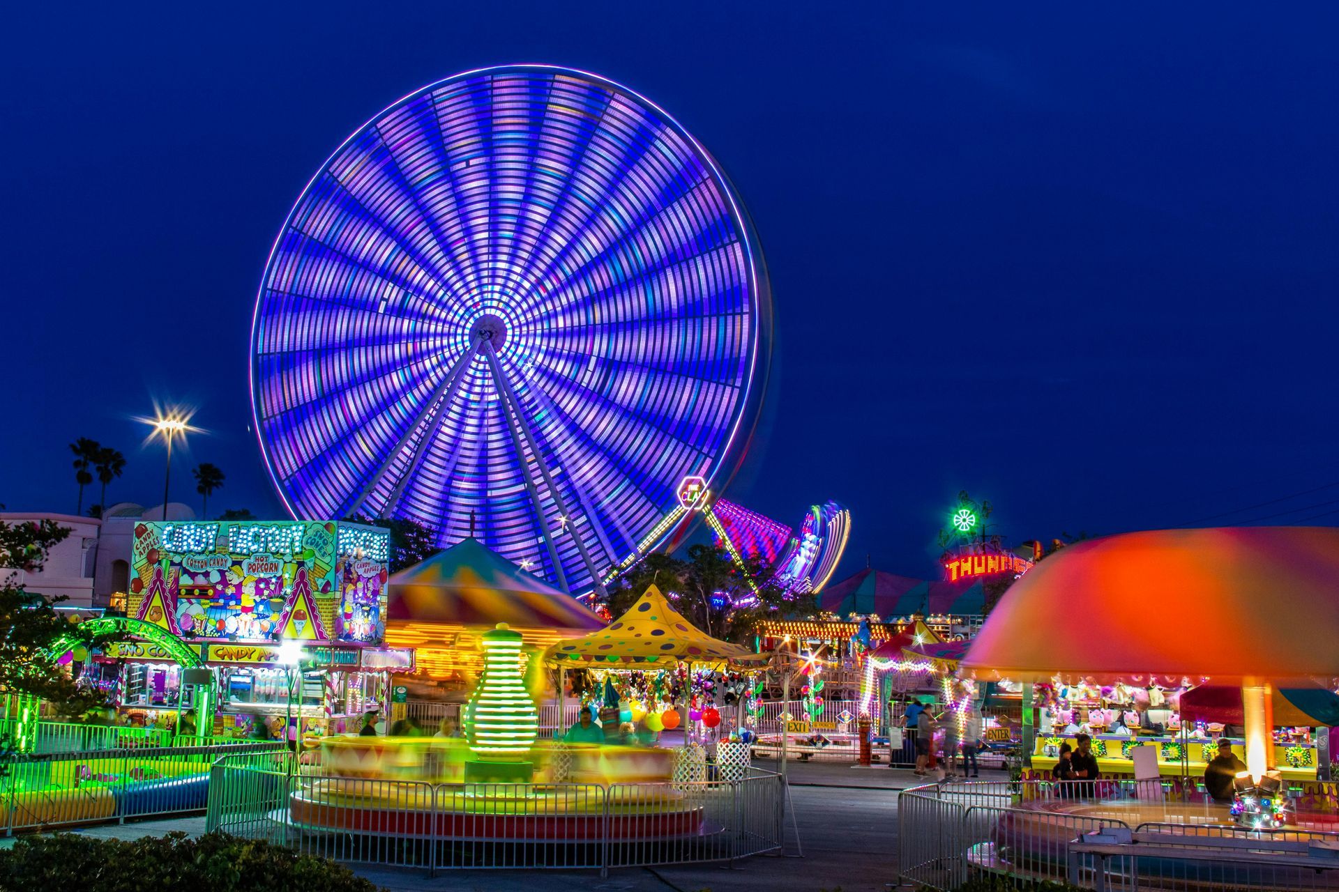 Nighttime carnival with a brightly lit Ferris wheel and various rides.