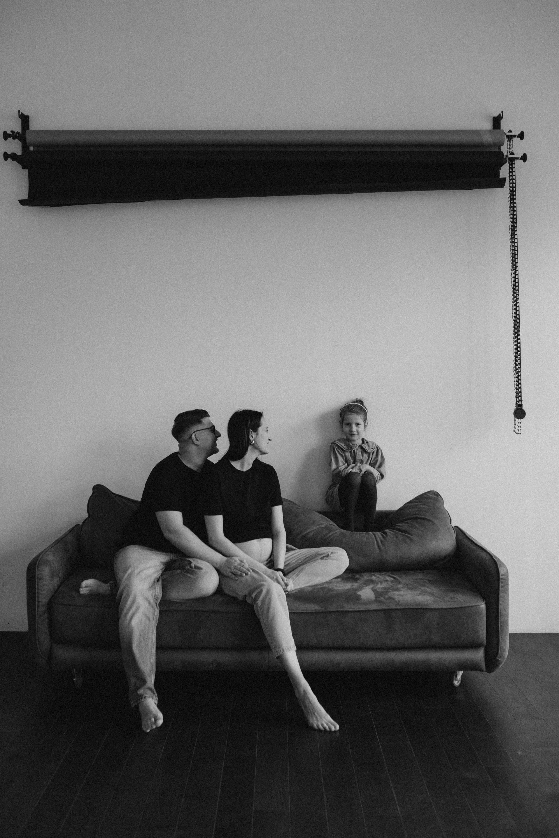 Family of three on a couch: two adults gazing at each other, child looking forward, black and white.