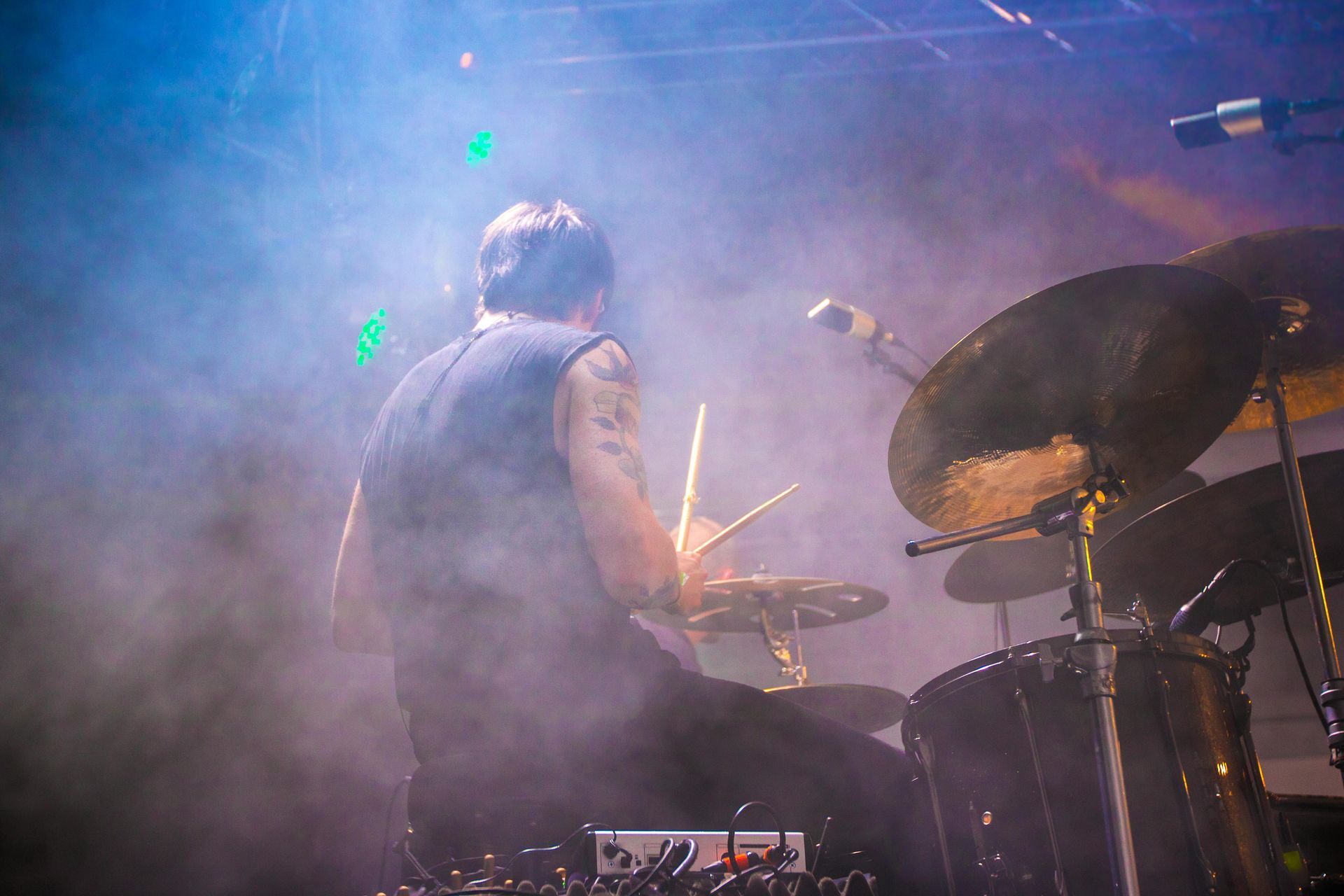 Drummer playing on stage, back to the camera, surrounded by smoke and stage lights.