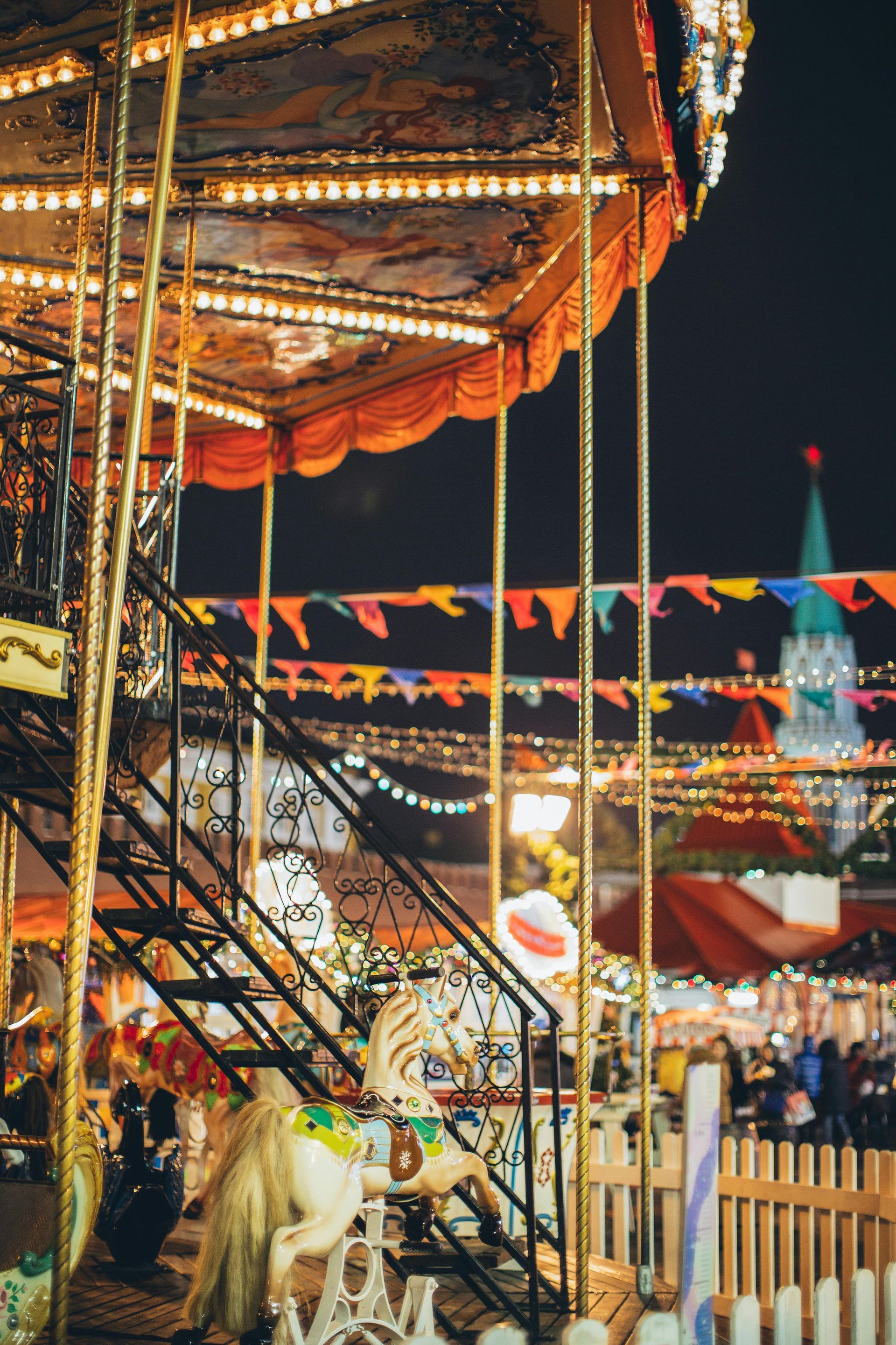 Carousel at night, lit with string lights, in front of a church with colorful flags.