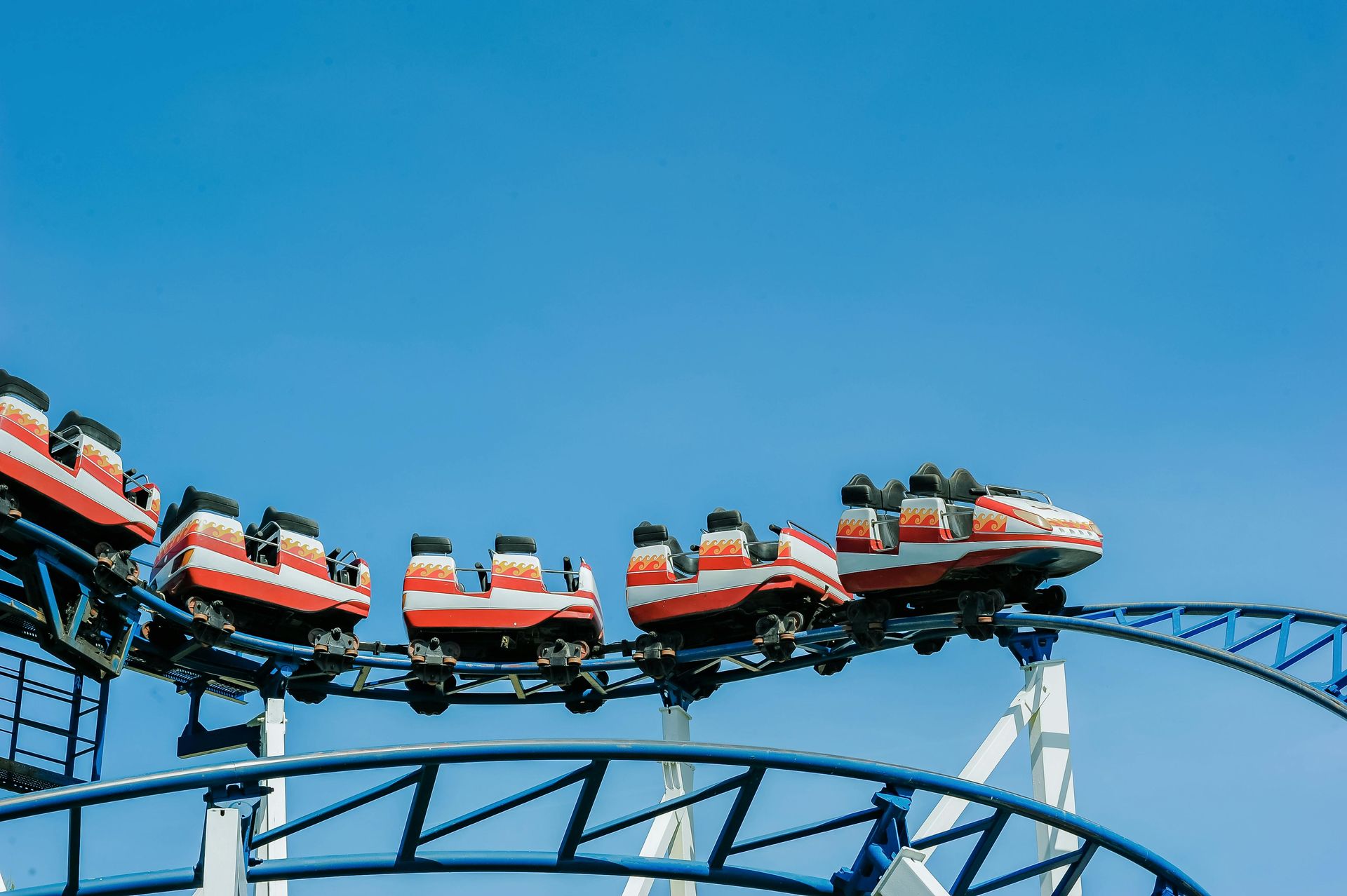 Roller coaster cars with orange and red accents on a blue track against a clear, blue sky.
