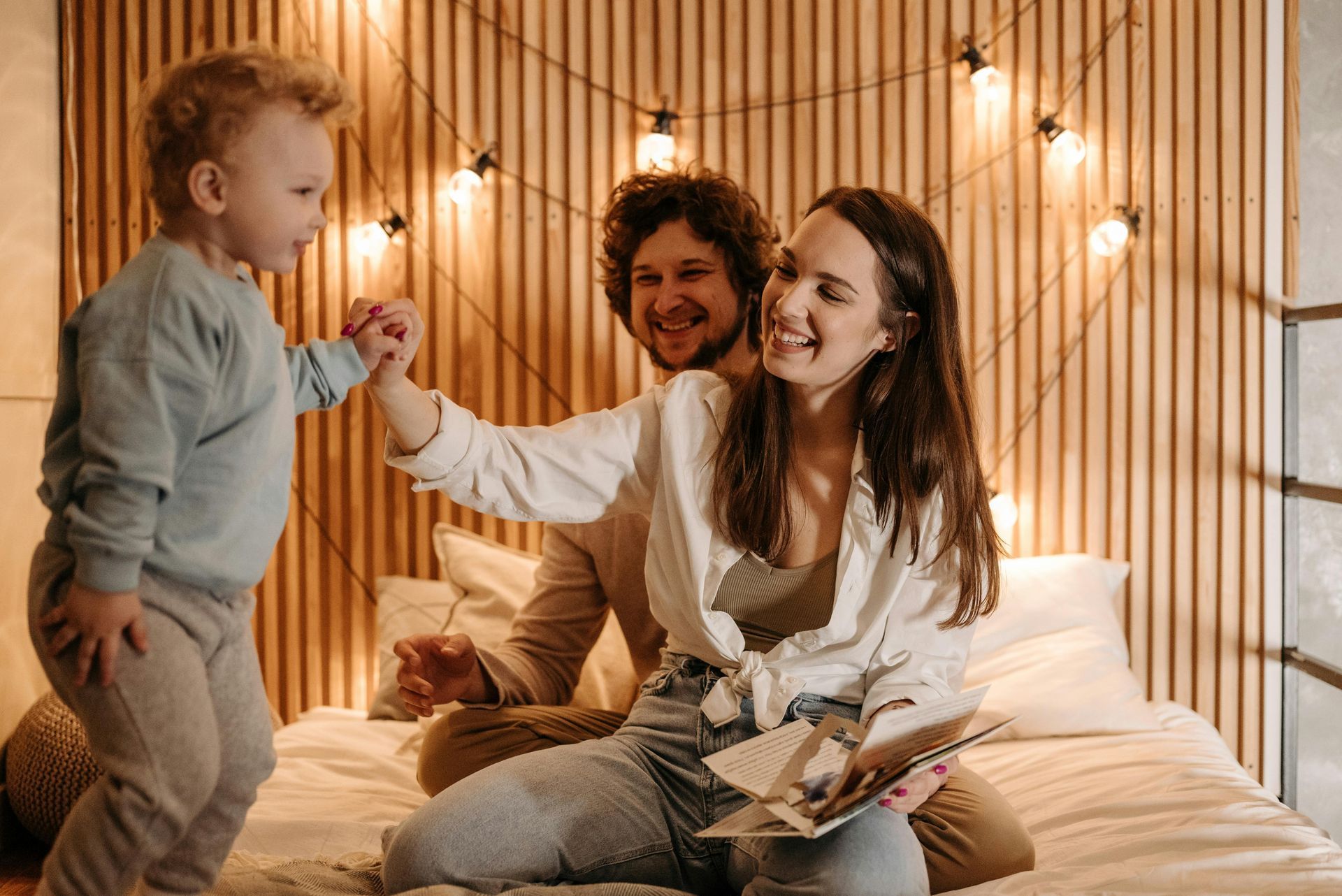 Family, including a child, on a bed with decorative lights, smiling and interacting.