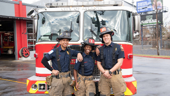 Three firefighters are posing for a picture in front of a fire truck.