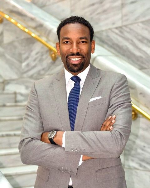 A man in a suit and tie is standing on a set of stairs with his arms crossed.