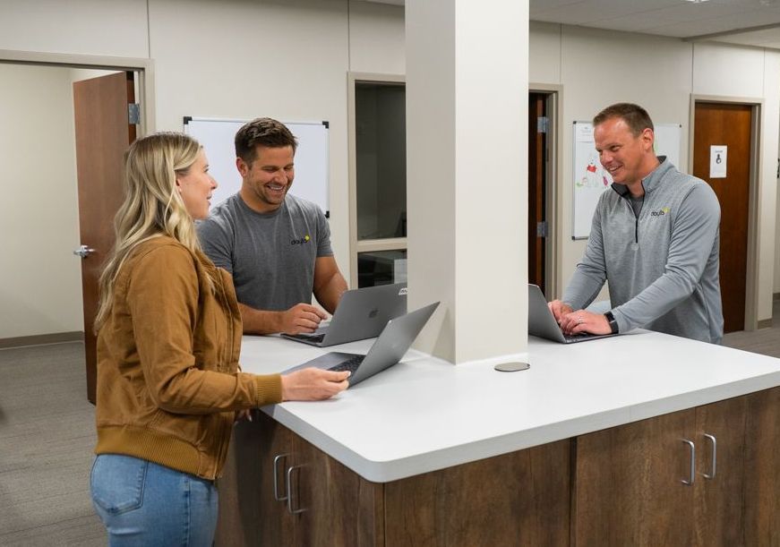 A group of people are standing around a table with laptops.