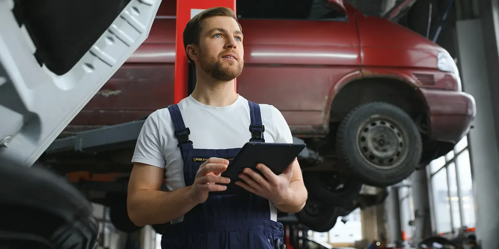 Mechanic with tablet inspecting a car raised on a lift in a workshop.