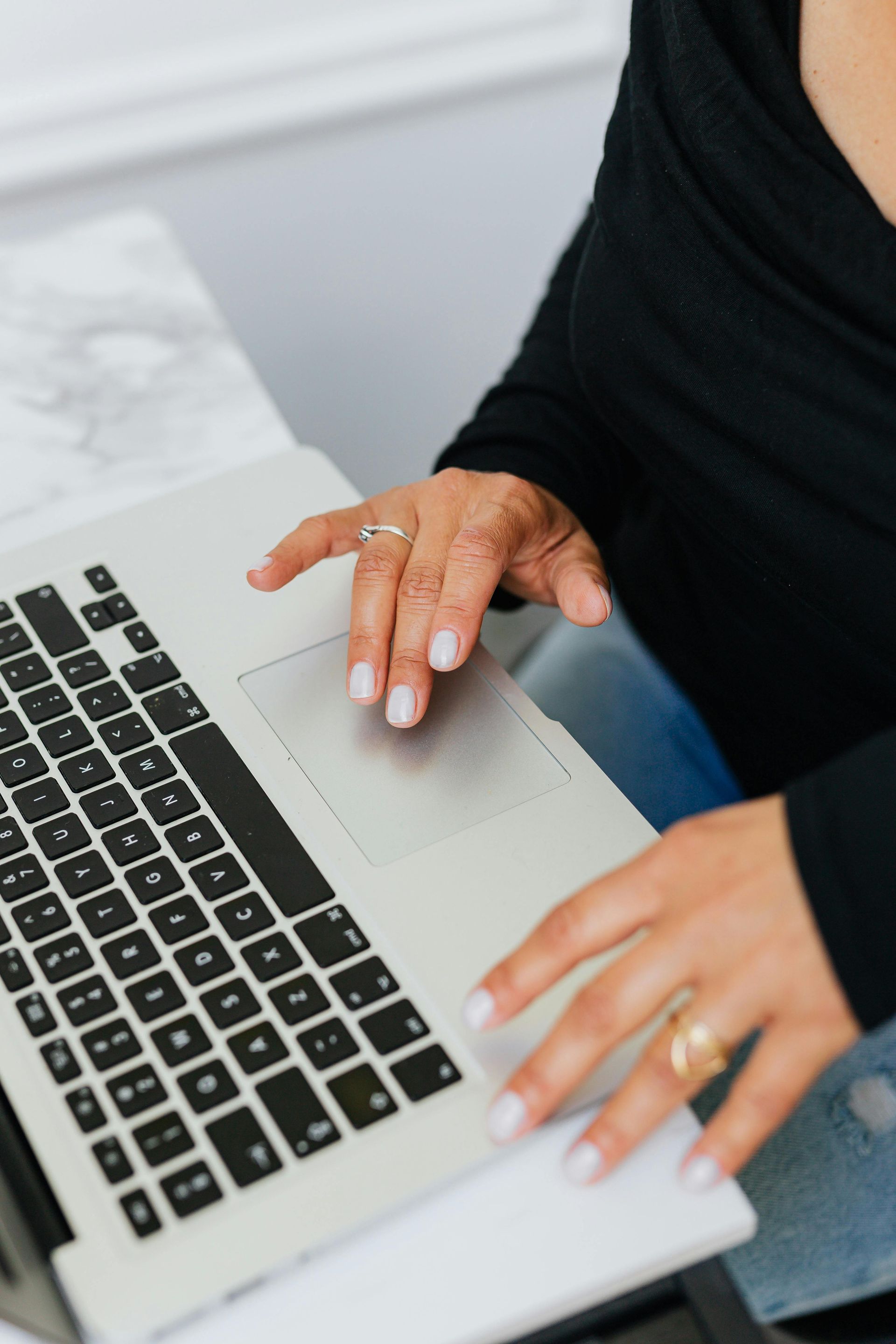 A woman is typing on a laptop computer with a ring on her finger.