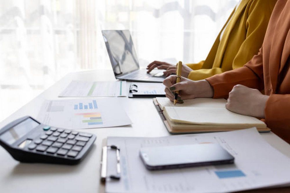 Two people are sitting at a table with a laptop and a calculator.