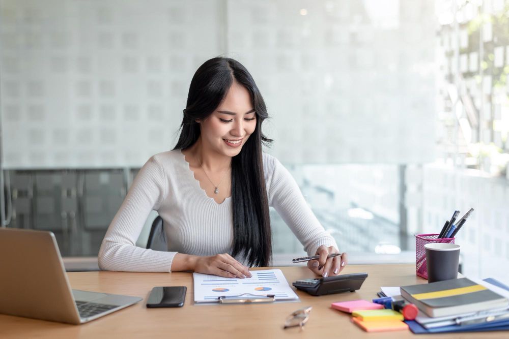 A woman is sitting at a desk with a laptop and a calculator.