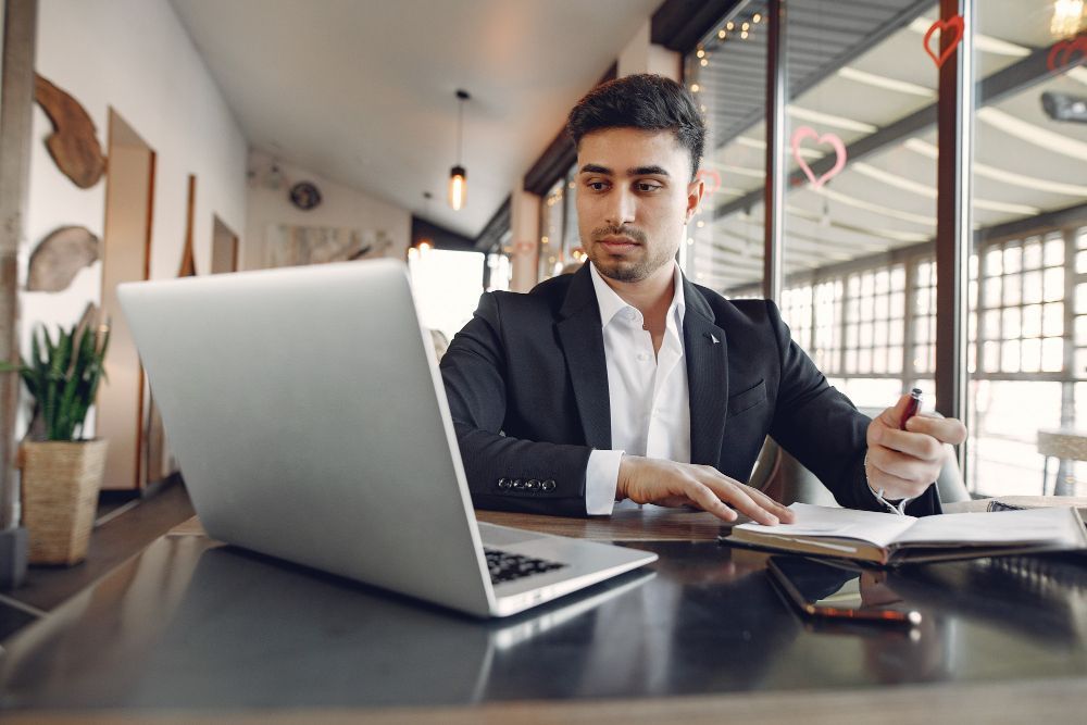 A man in a suit is sitting at a table using a laptop computer.