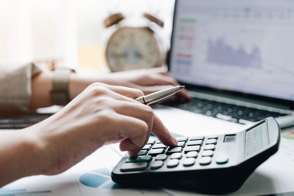 A person is using a calculator in front of a laptop computer.