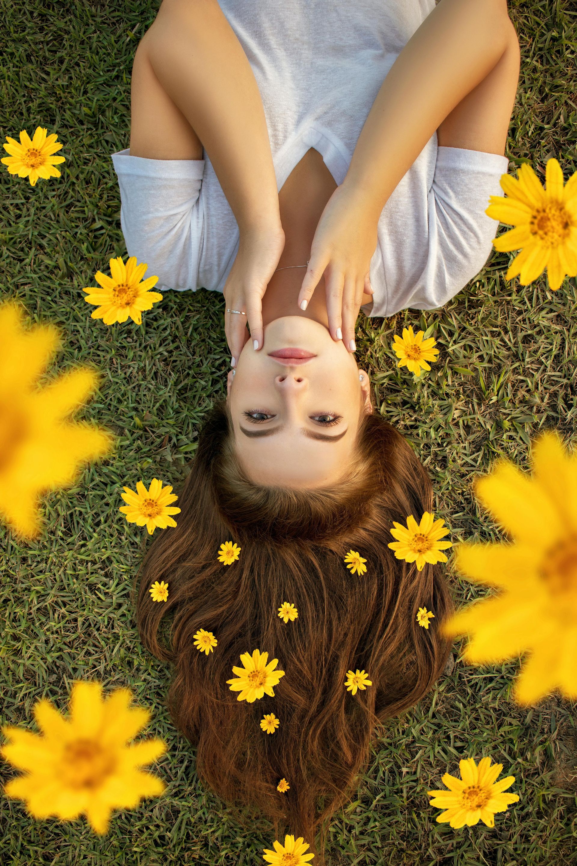 A woman is laying on her back in the grass surrounded by yellow flowers.