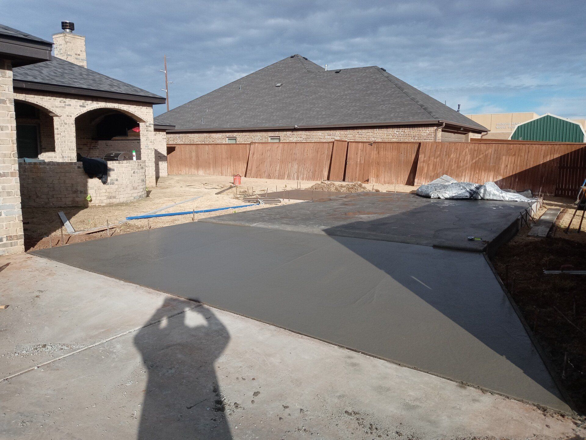 A shadow of a person is cast on a concrete driveway in front of a house.