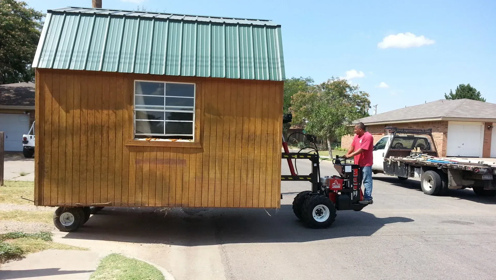 A man is pushing a small wooden house on a trailer