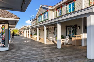 Boardwalk storefronts with white columns, striped awnings, and outdoor seating under a bright blue sky