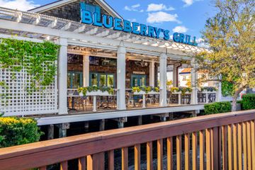 Blueberry Grill restaurant patio with white pergola, blue sign, and outdoor seating in sunlight