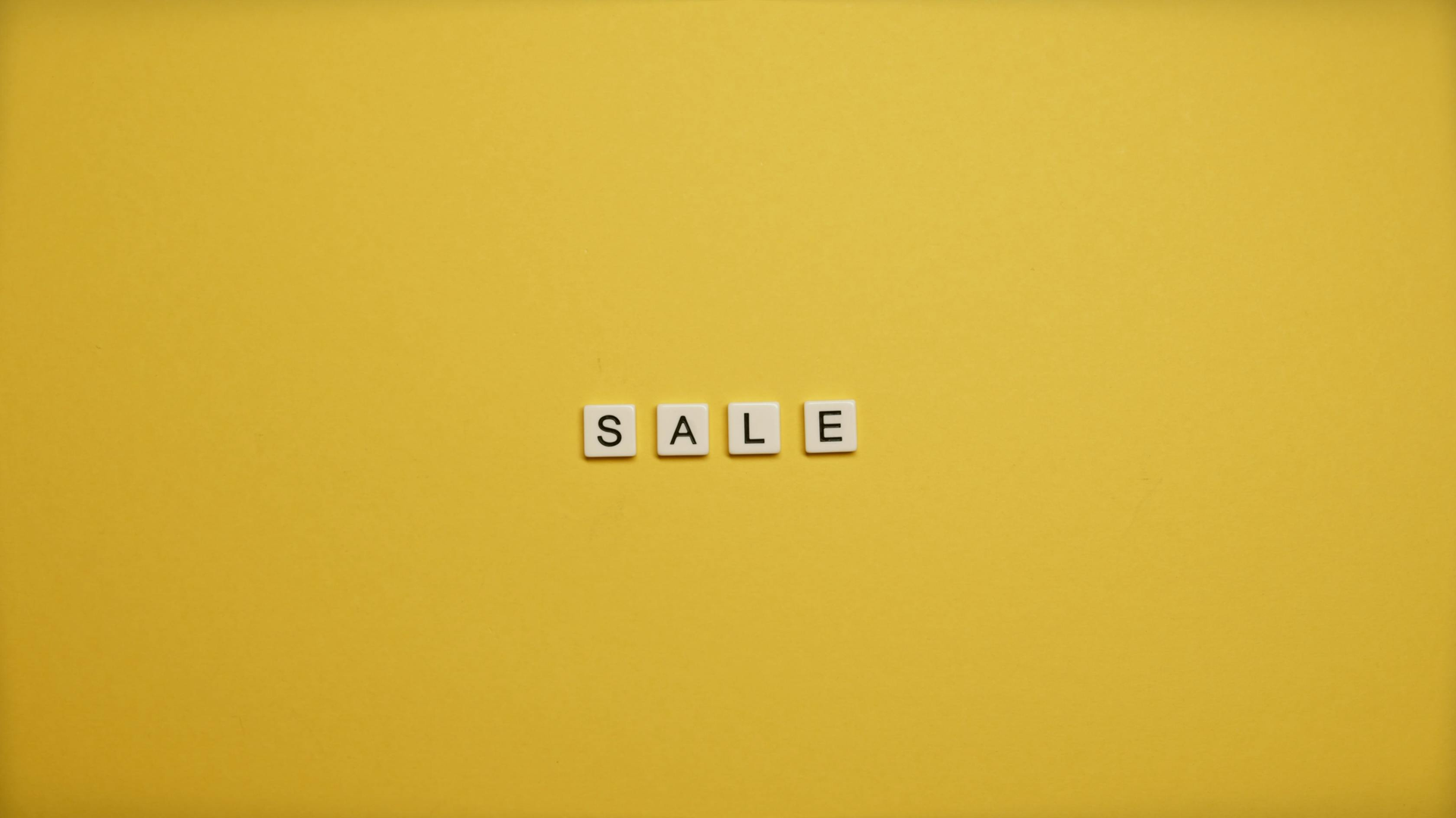 “SALE” spelled with letter tiles on a bright yellow background.