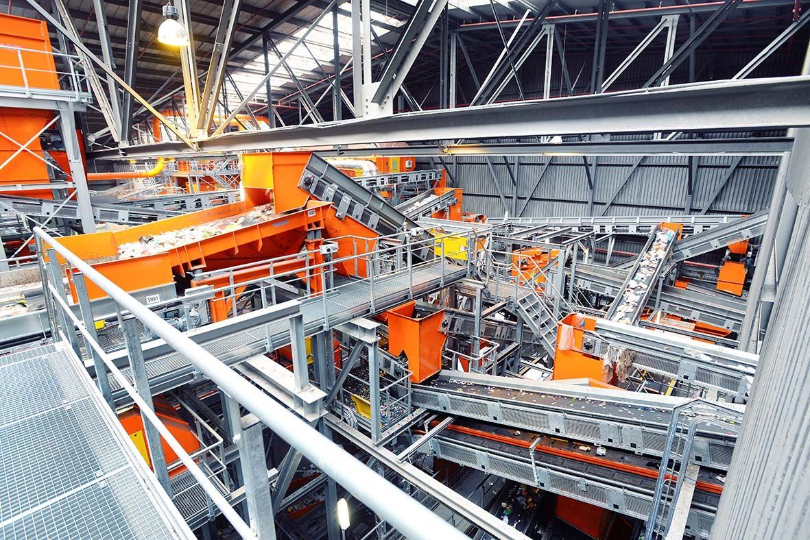 Industriële recyclingfabriek met oranje en grijze machines. Transportbanden transporteren materialen.