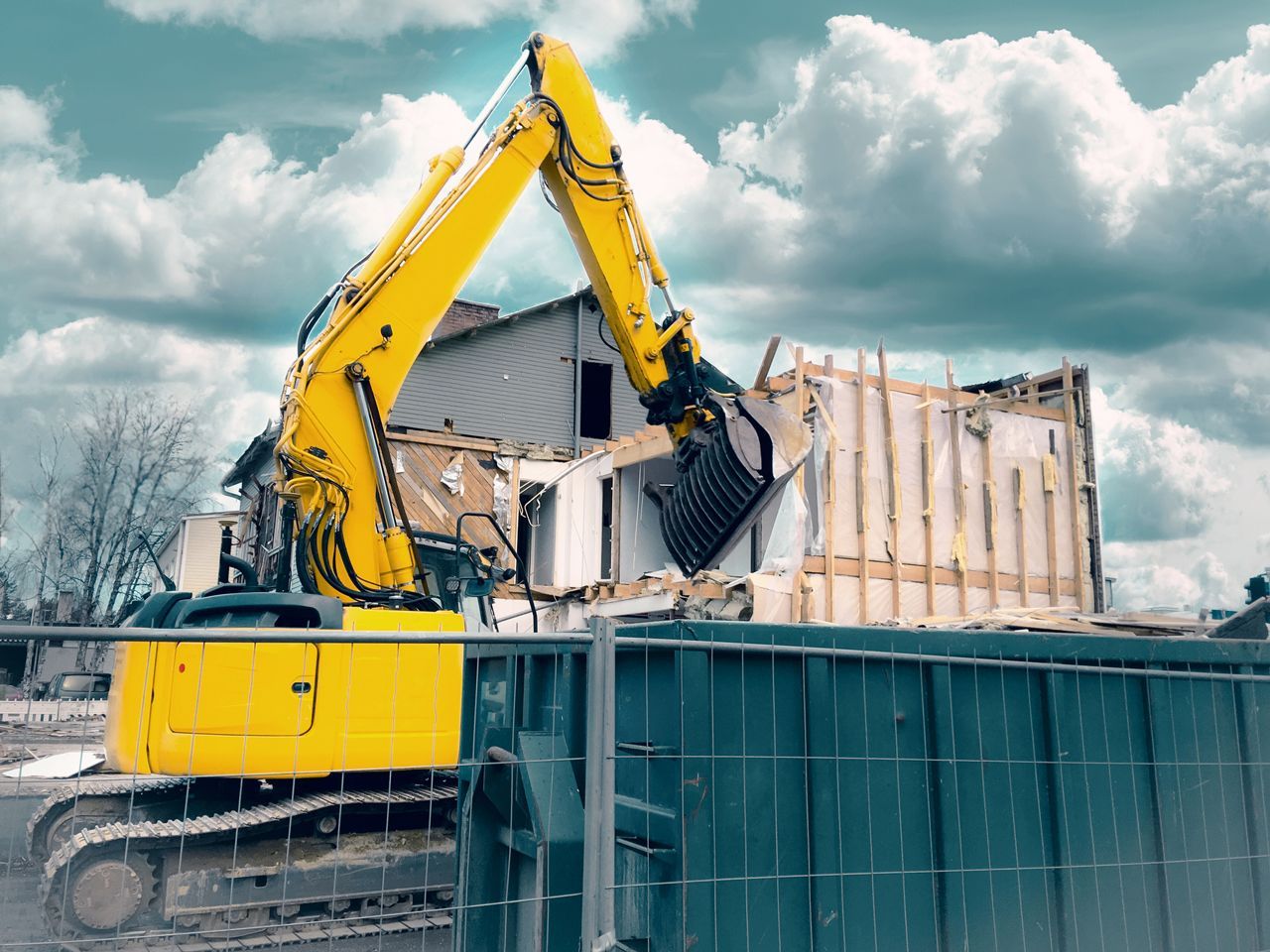 A yellow excavator is demolishing a house on a construction site.