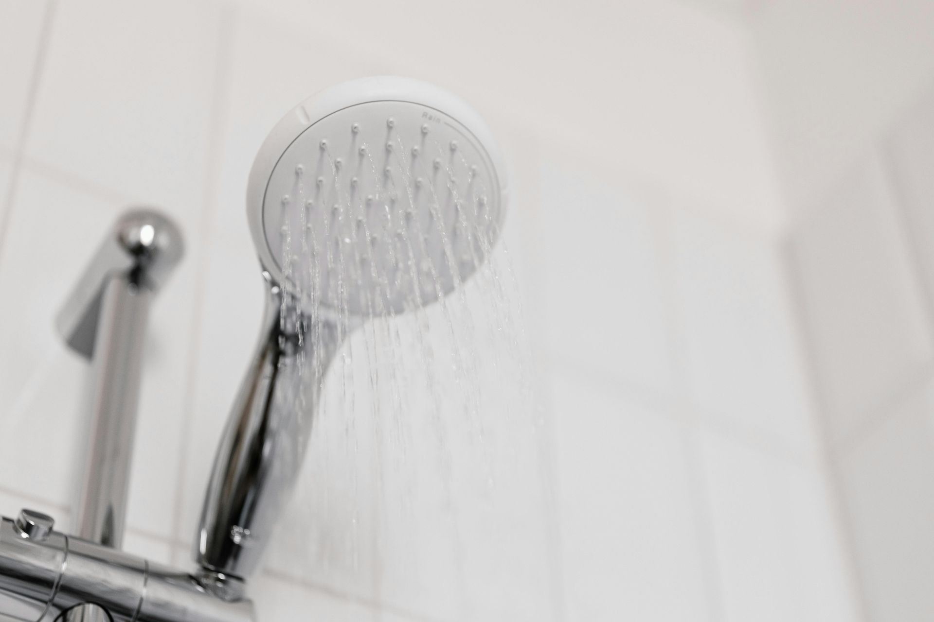 A chrome shower head sprays water against a white tiled wall.