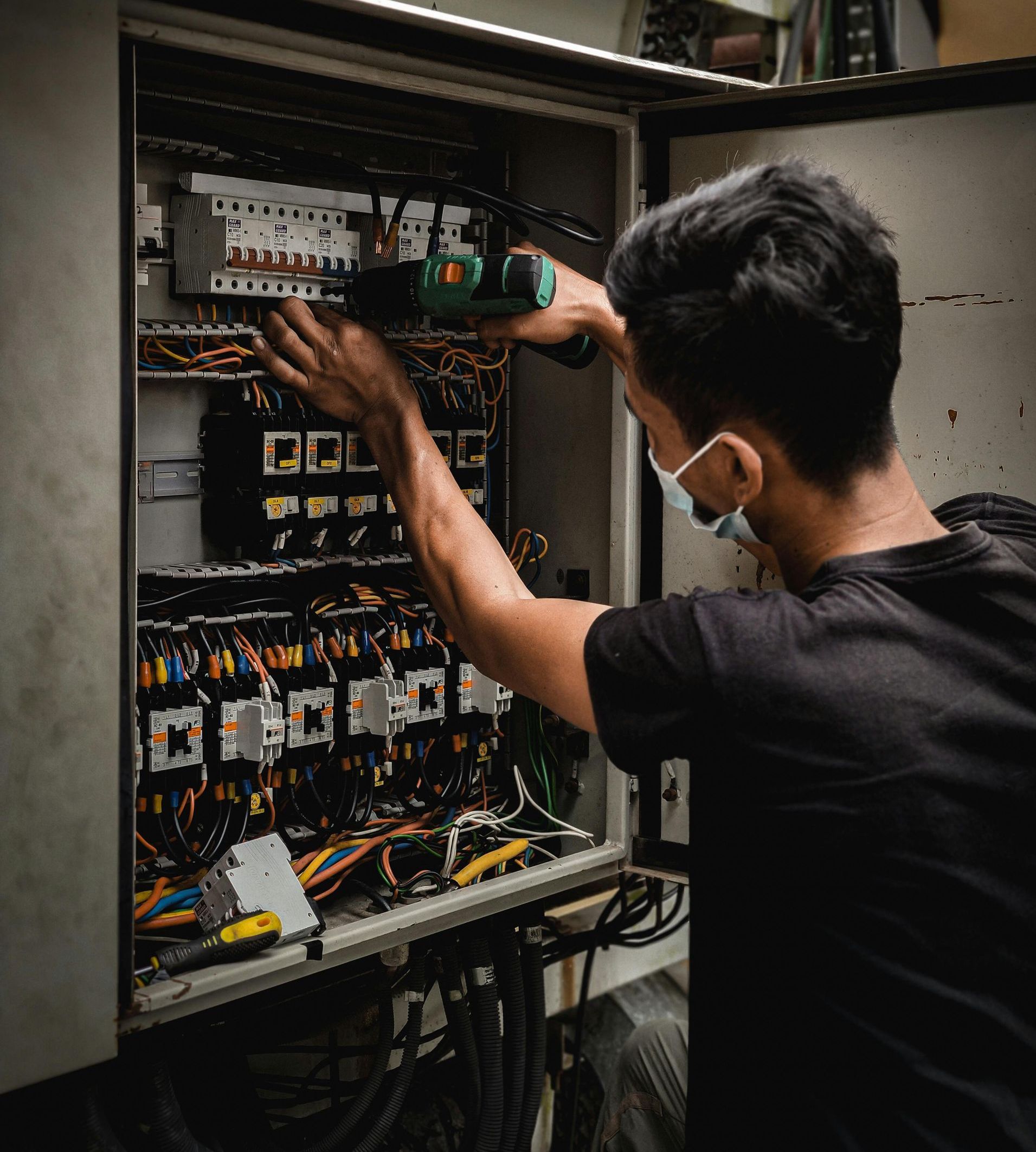 A man wearing a mask is working on an electrical box.