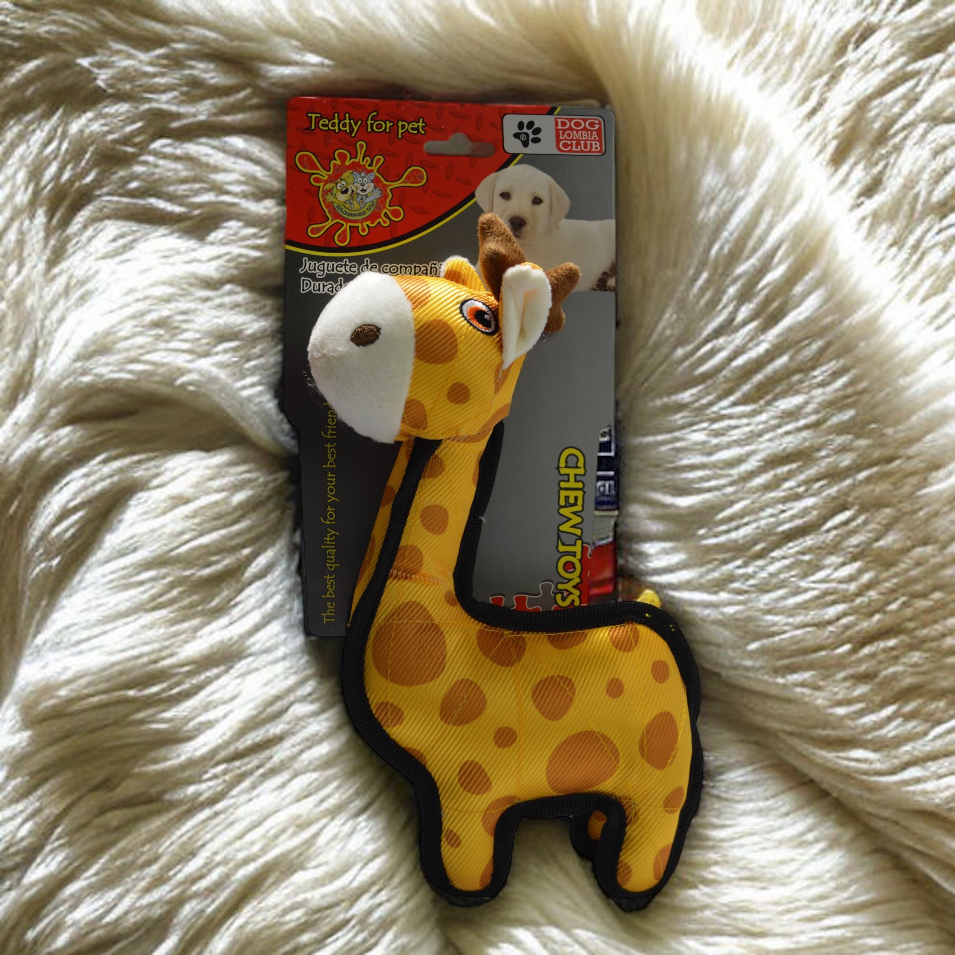 Juguete para perros: una jirafa amarilla con manchas marrones sobre una superficie blanca esponjosa junto al embalaje.