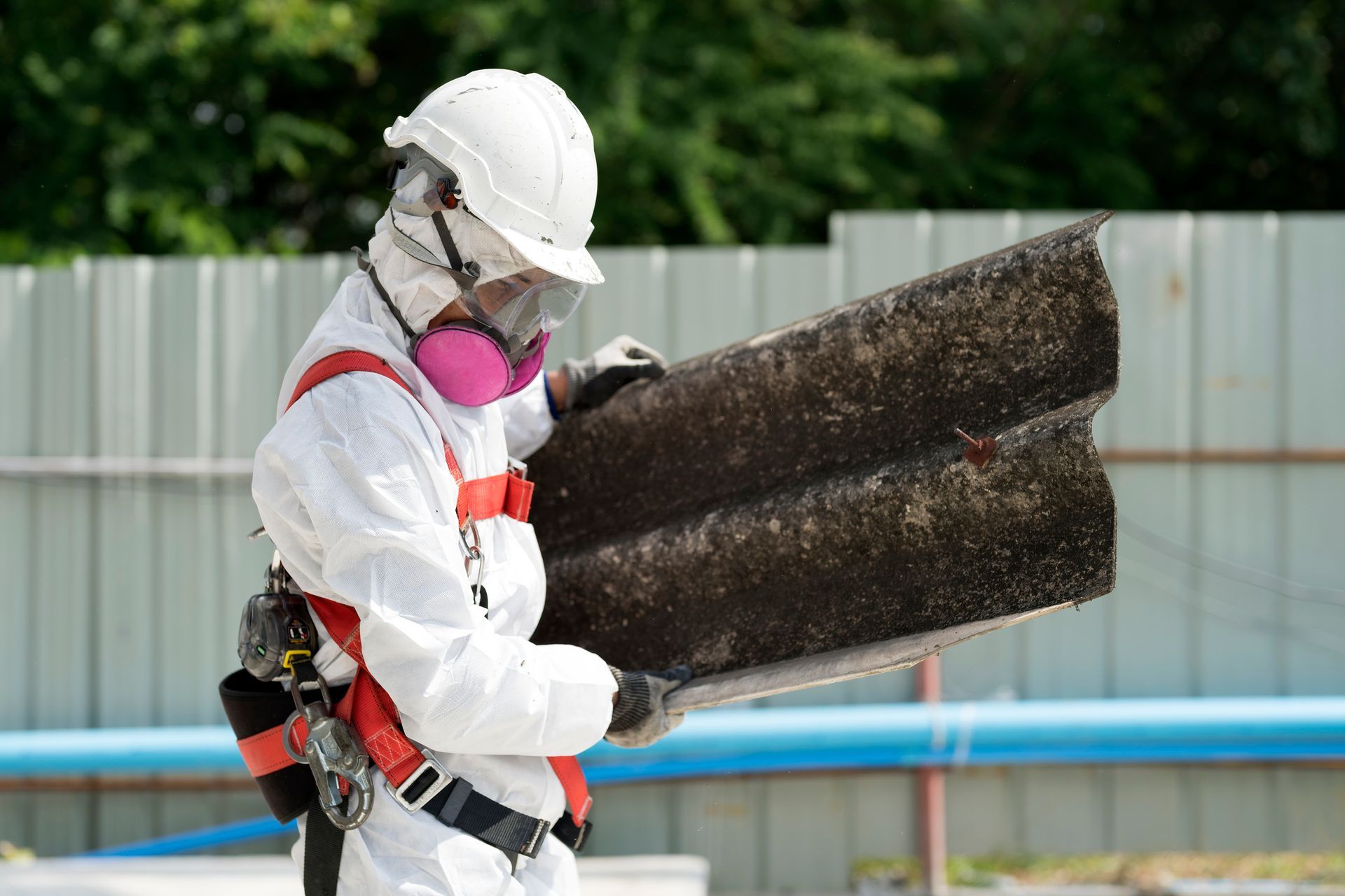 Asbestos removal worker in full protective gear handling hazardous materials safely at job site.