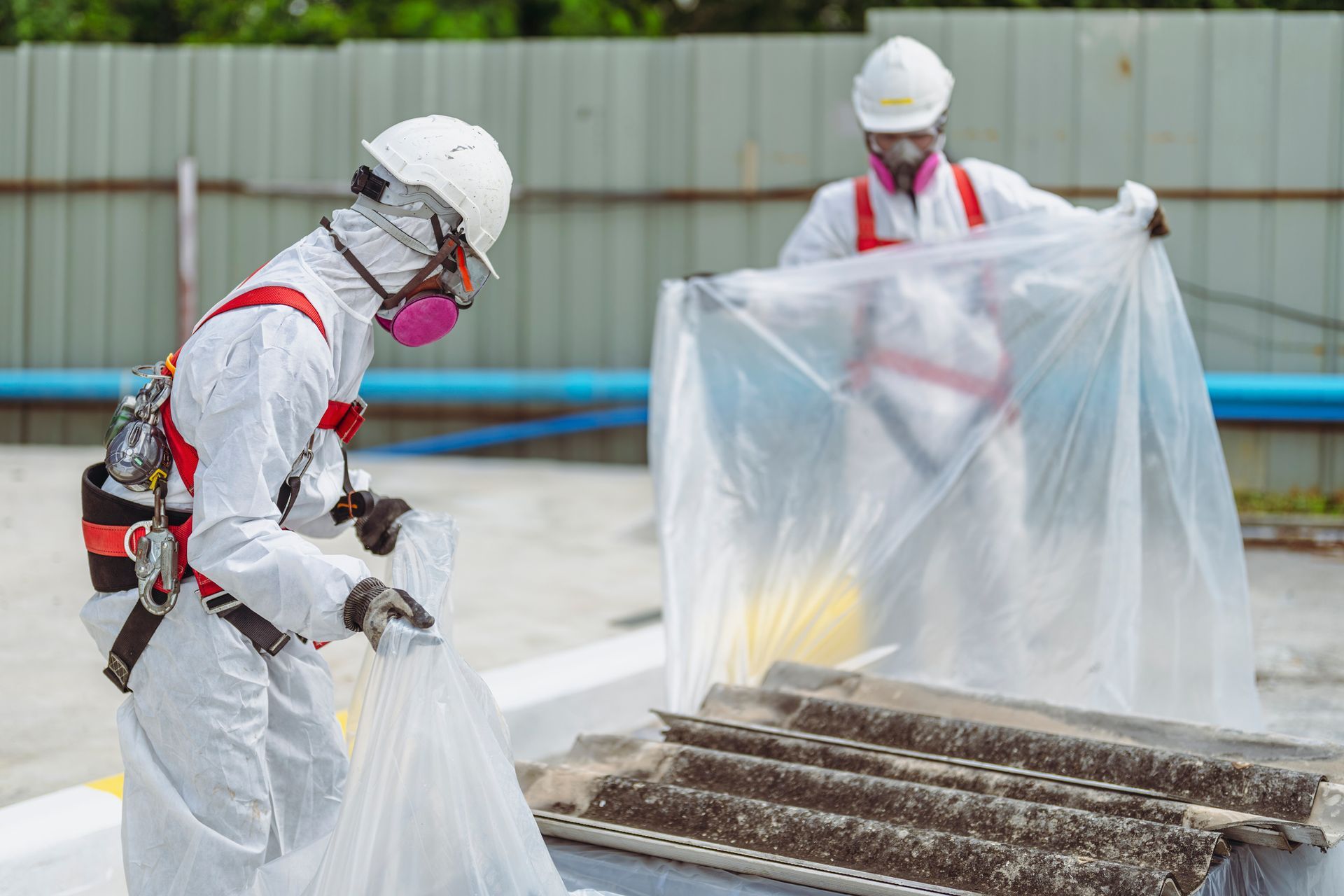 Asbestos removal workers in full protective suits safely handling hazardous materials outdoors. Asbestos removal workers in full protective suits safely handling hazardous materials outdoors.