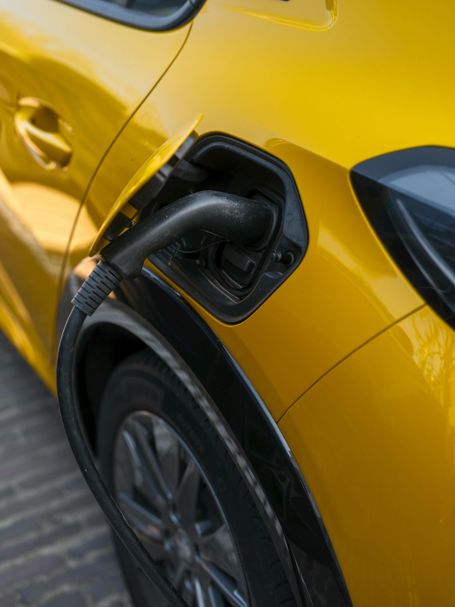 Yellow electric car charging, black charging cable plugged into the car's side.