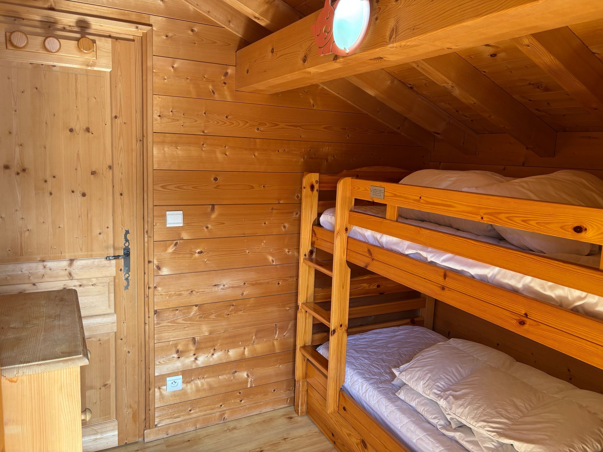 Wooden bunk beds inside a wood-paneled room with a door and small window.
