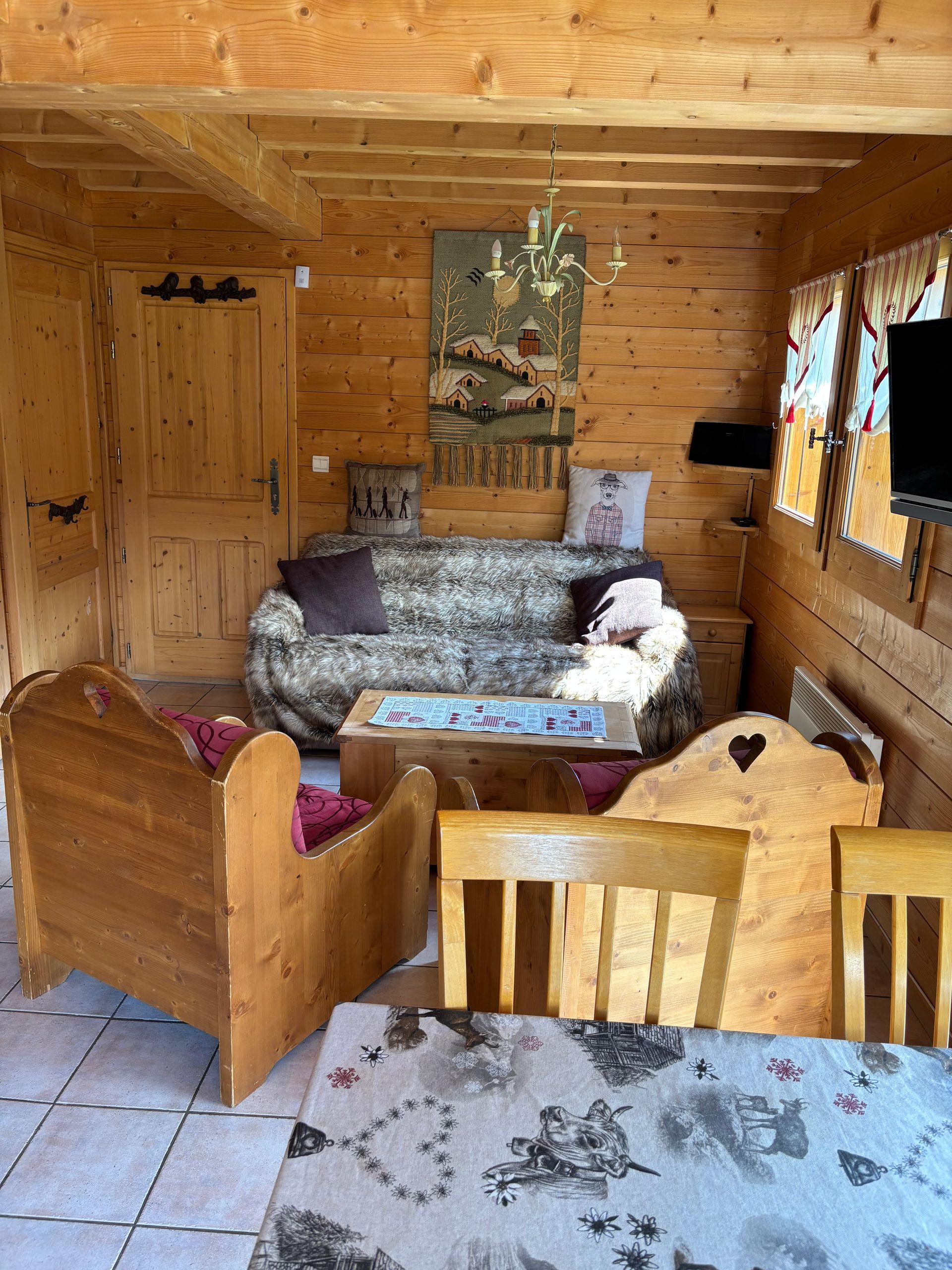 Cozy wooden cabin interior with sofa, table, chairs, and tapestry.