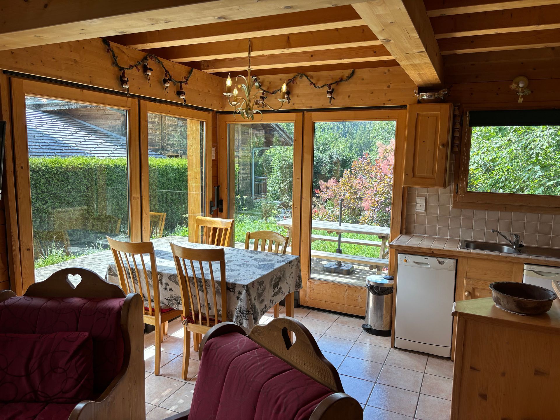 Cozy dining area with wooden beams, a table set for six, and a view of a garden through large windows.