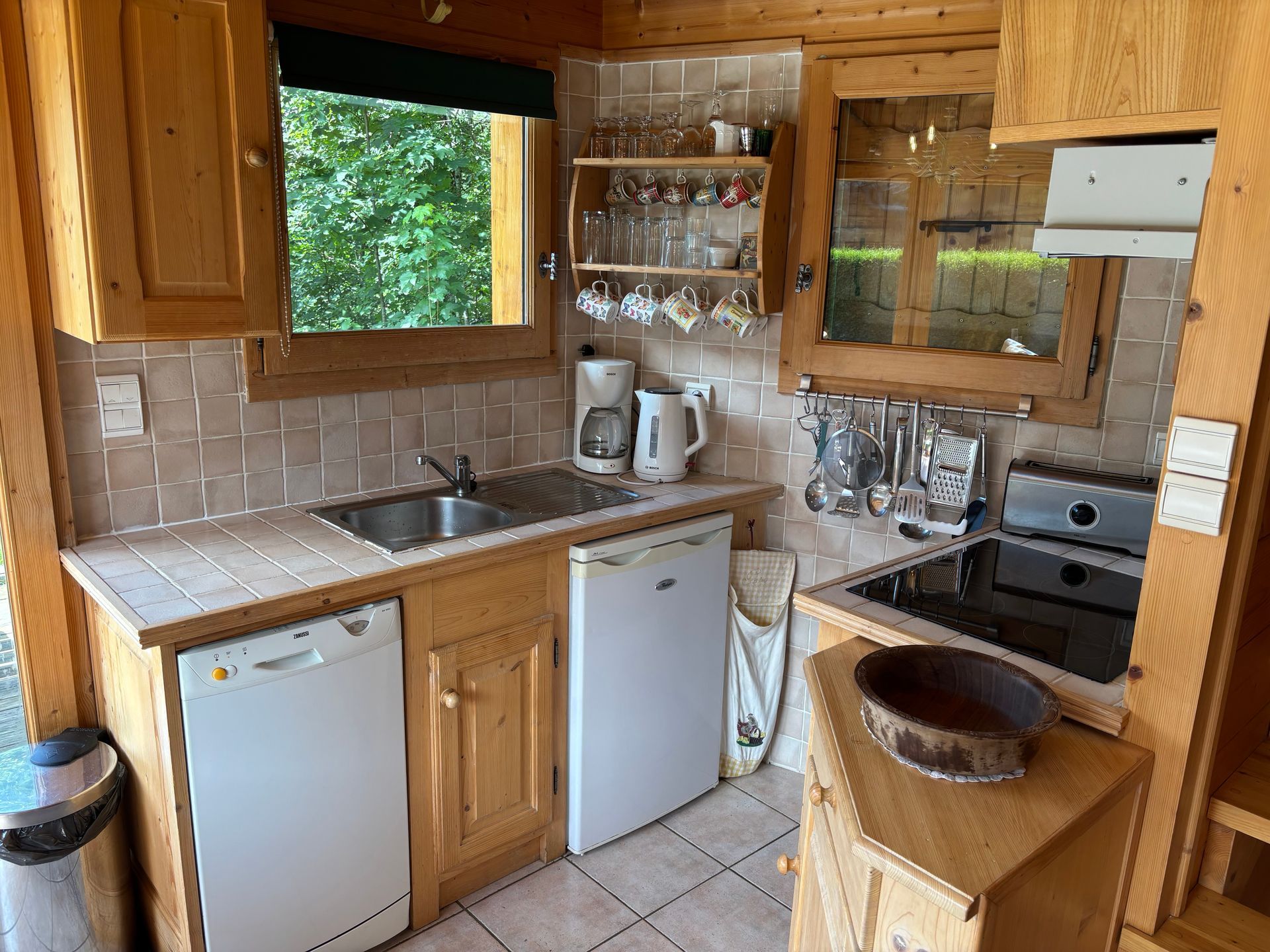 Small wooden cabin kitchen with appliances, cabinets, and a window.