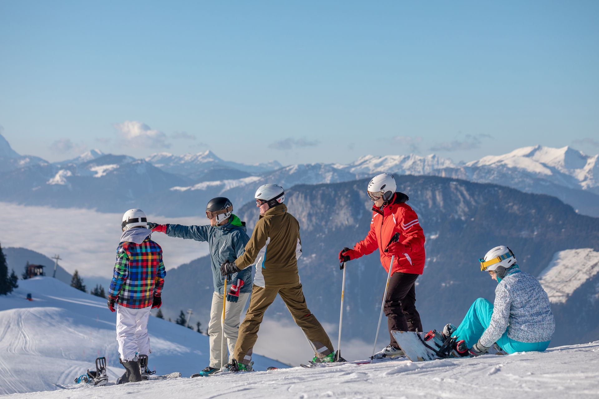 People on skis and a snowboard enjoy mountain views on a sunny day.