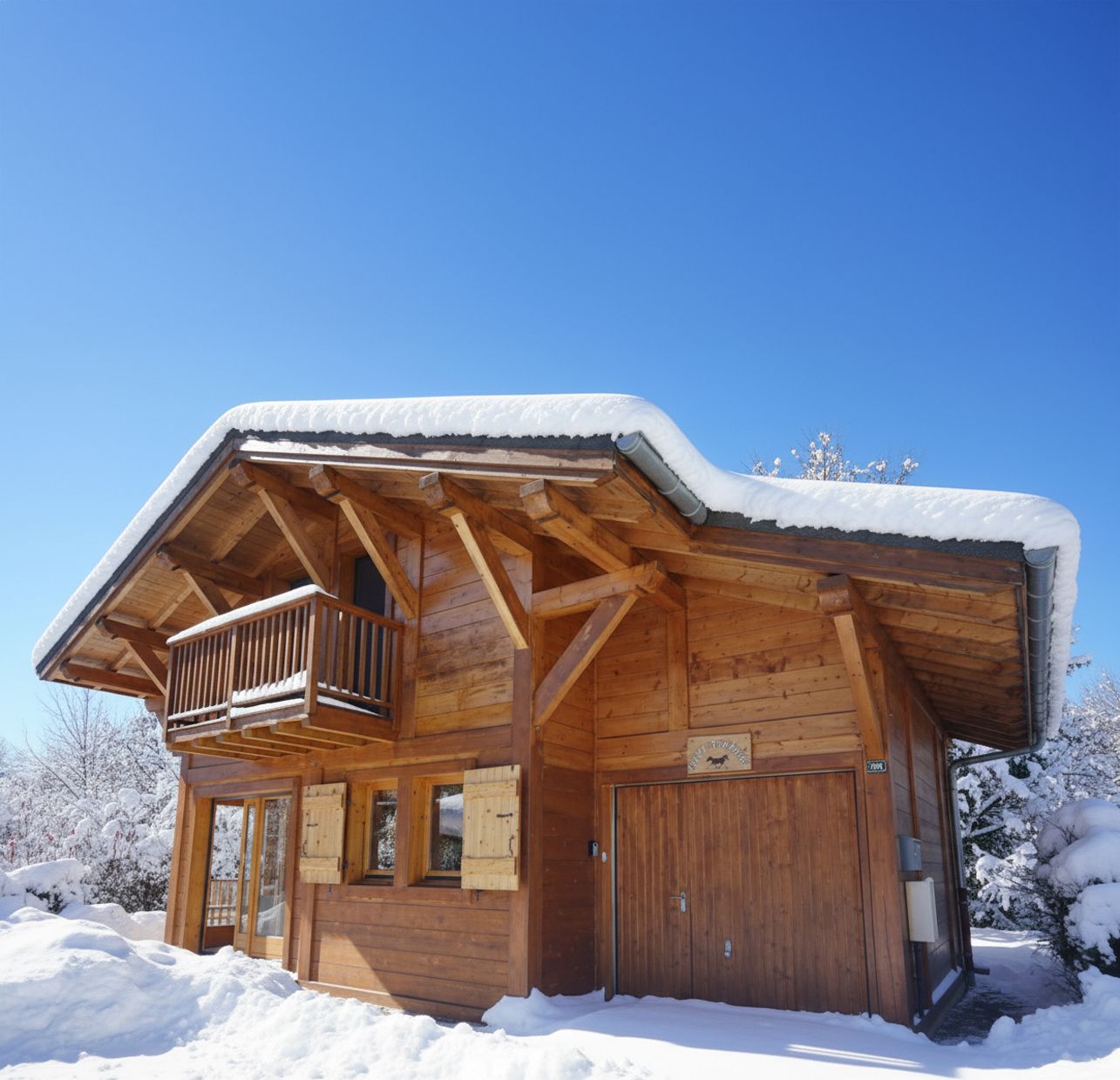 Wooden chalet covered in snow under a bright blue sky, with a balcony and closed shutters.