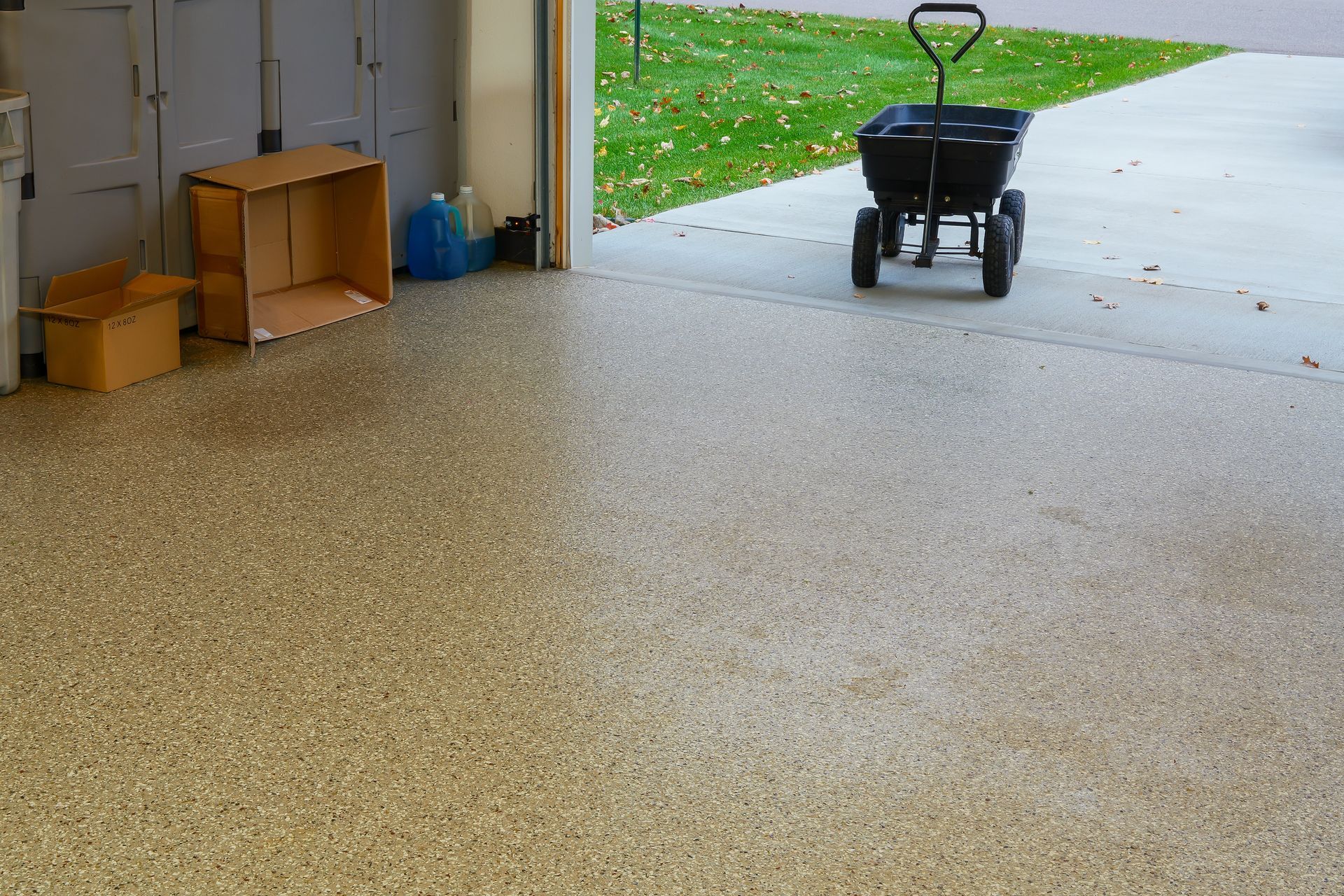 Garage with speckled floor, cardboard boxes, and a black hand truck by the open doorway.