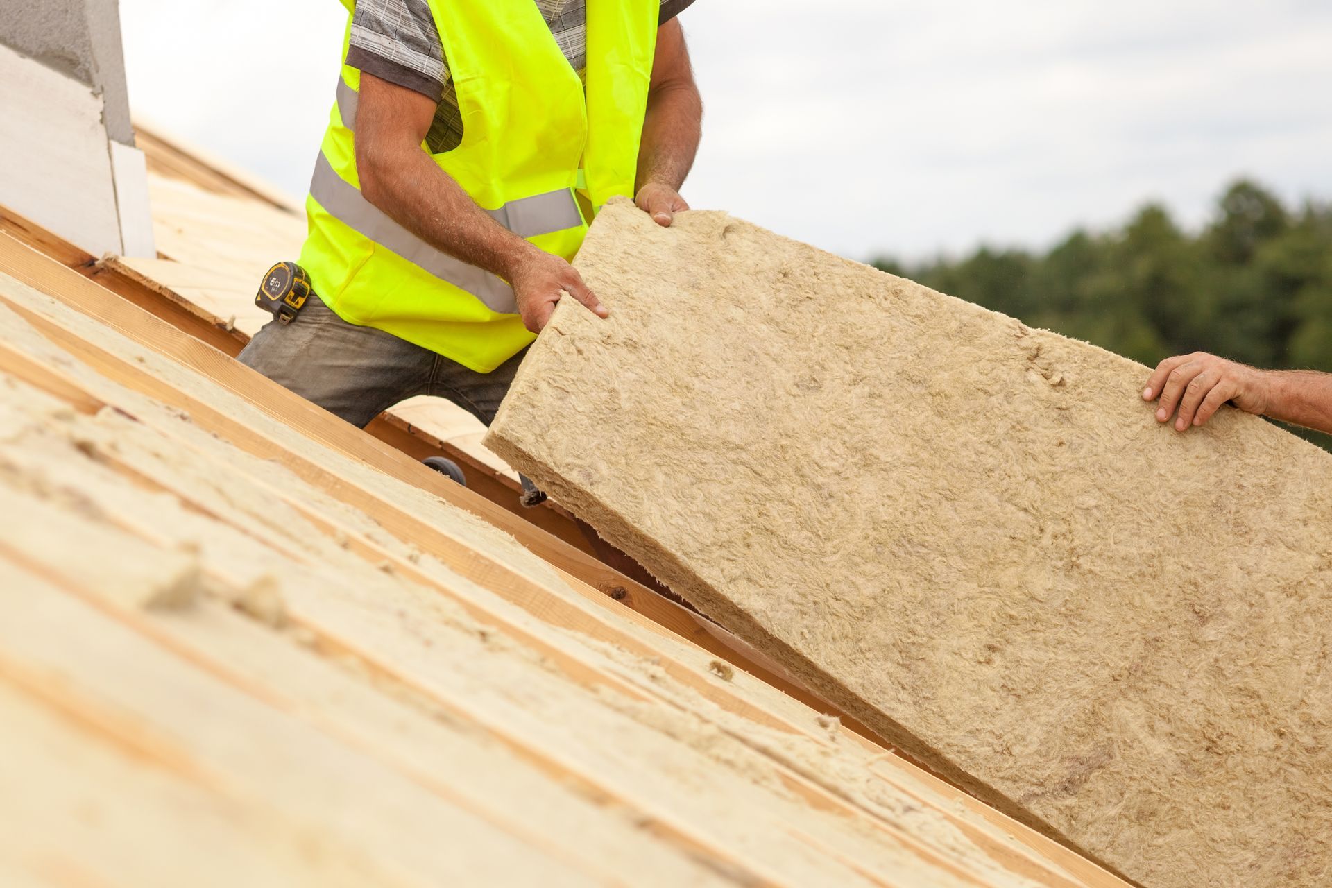 Une personne en gilet jaune installe une isolation sur un toit en bois.