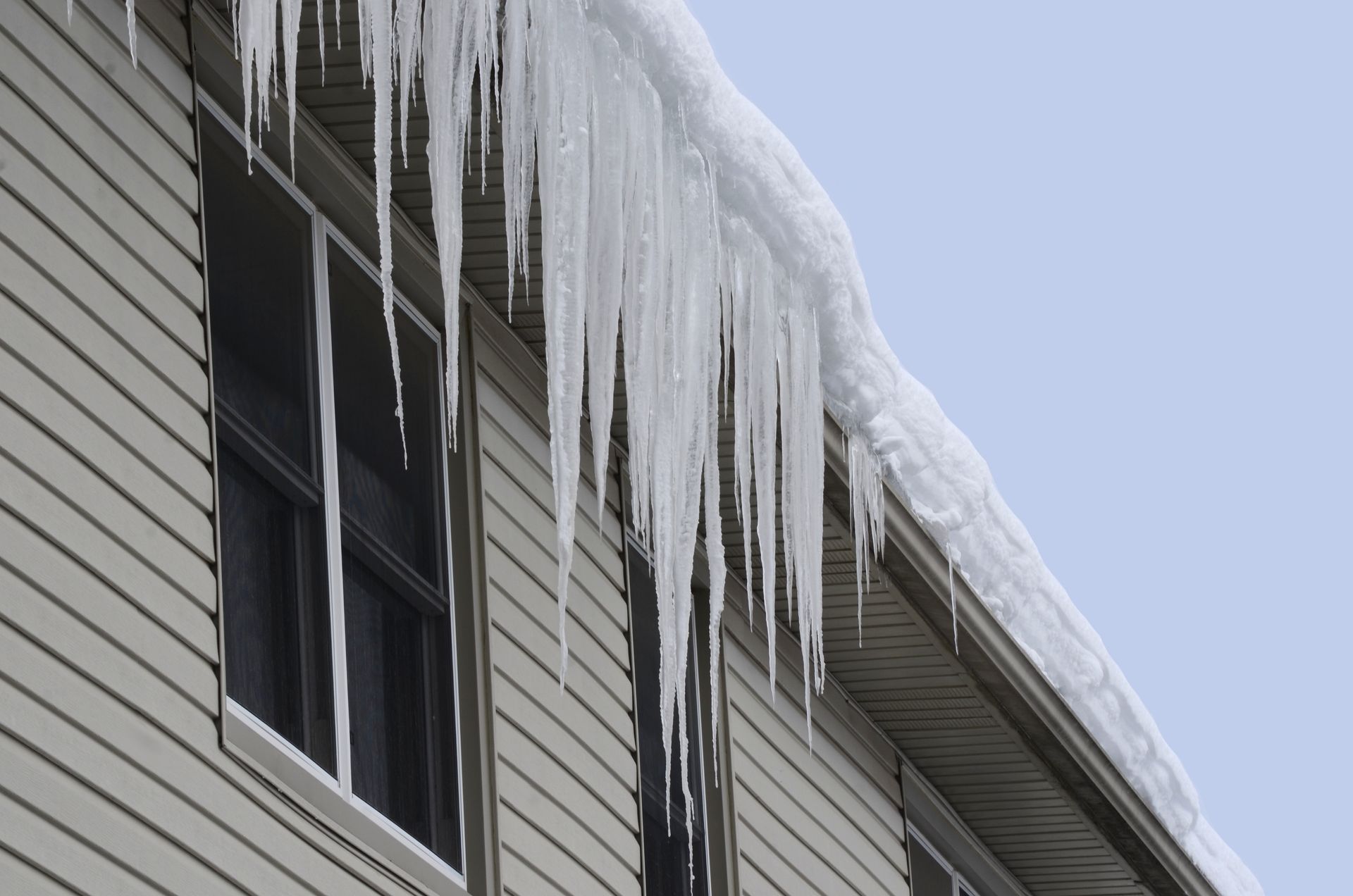 Des glaçons suspendus au toit d'une maison, au-dessus d'une fenêtre, par temps nuageux.