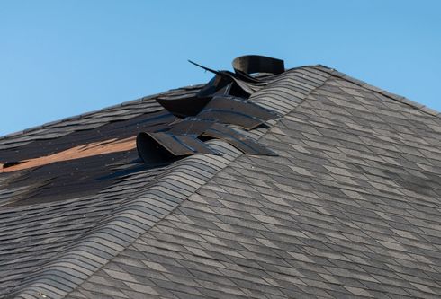 Toiture endommagée avec bardeaux manquants, asphalte, contre un ciel bleu.