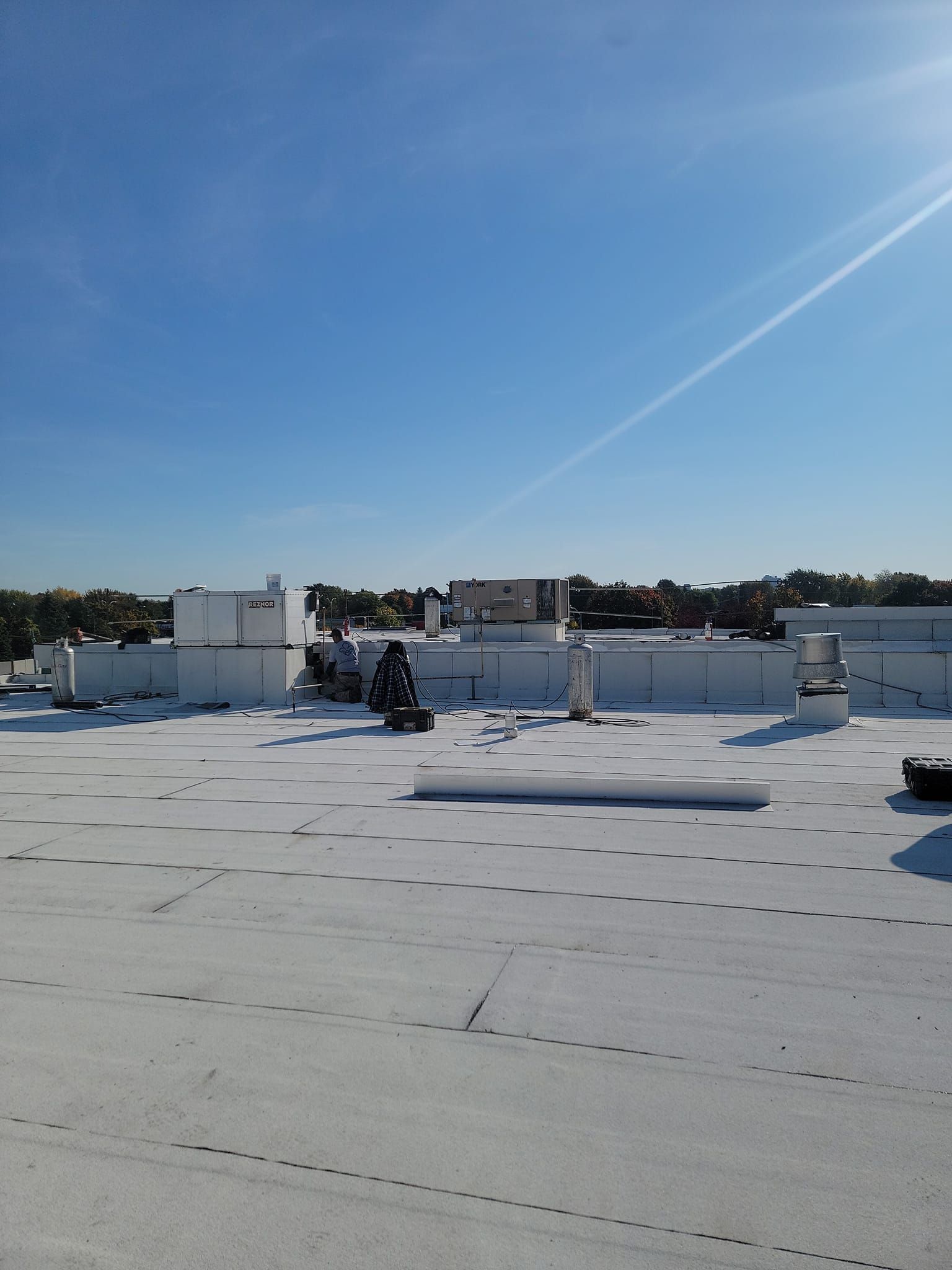A flat, white commercial roof with equipment under a clear blue sky.