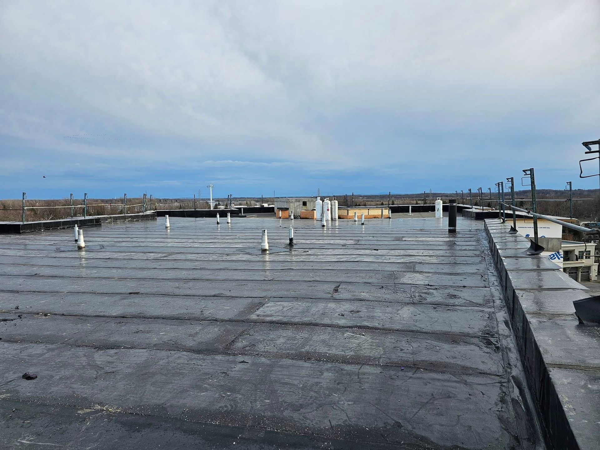 Toit plat sous un ciel nuageux ; plusieurs tuyaux et matériaux de construction visibles.