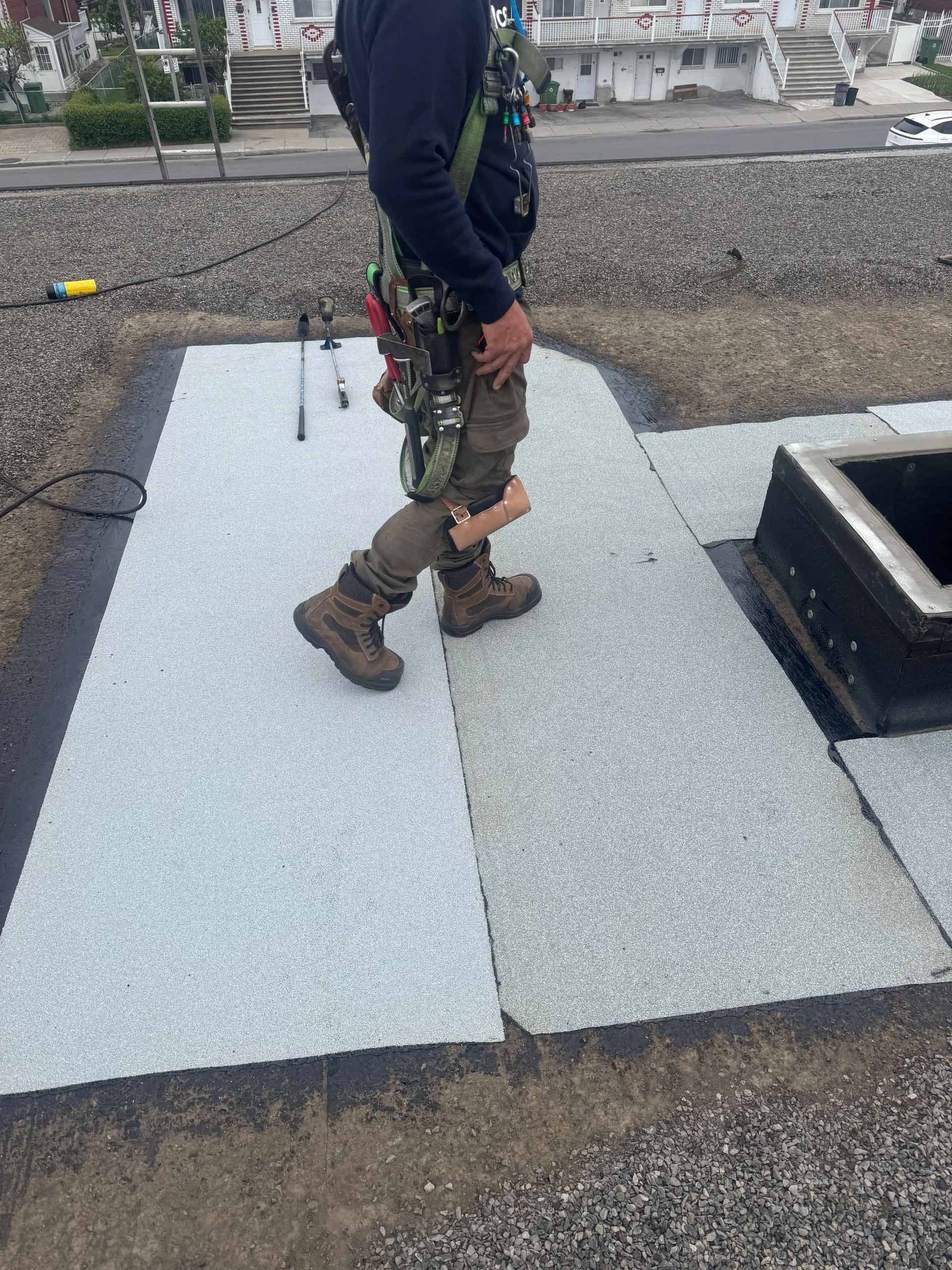 Couvreur en harnais de sécurité sur un toit plat en tuiles de pierre grise.