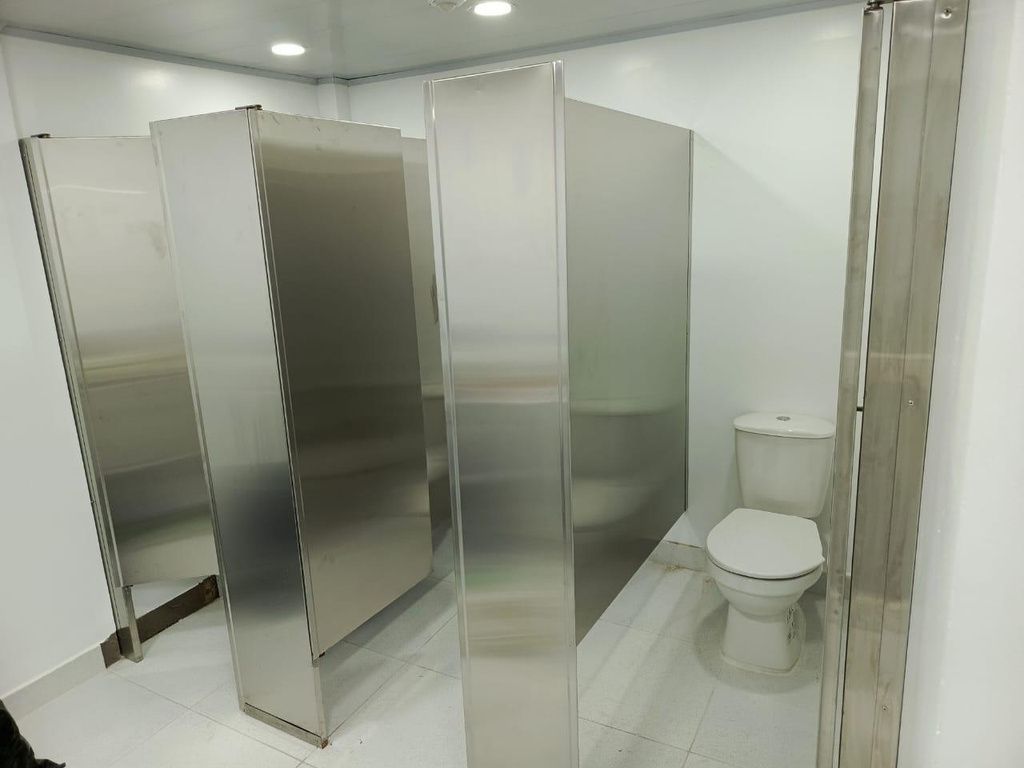 Baño público con cabinas de acero inoxidable e inodoro blanco.