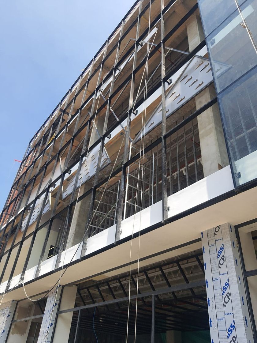 Edificio de varias plantas en construcción con fachada de vidrio y metal.