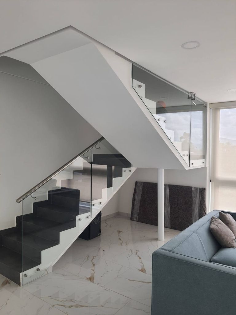 Escalera de caracol interior con escalones de piedra gris y barandilla de cristal, vista desde arriba.