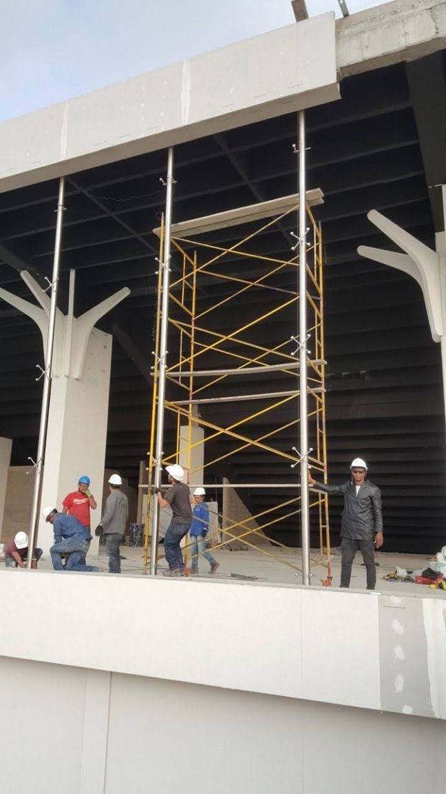 Obreros de la construcción utilizando andamios bajo el alero blanco de un edificio.