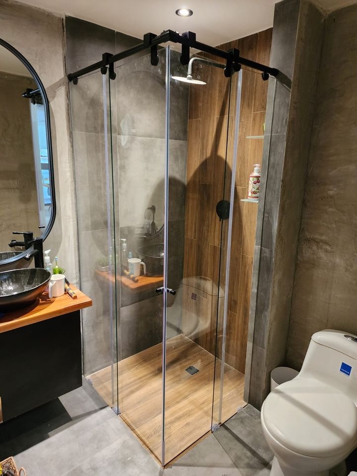 Baño público con paneles de privacidad blancos esmerilados, urinarios de acero inoxidable y suelo de baldosas negras.